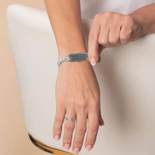 Woman wearing a light blue wrap-style medical ID bracelet with a silver-tone emblem plate, combining everyday comfort and safety.