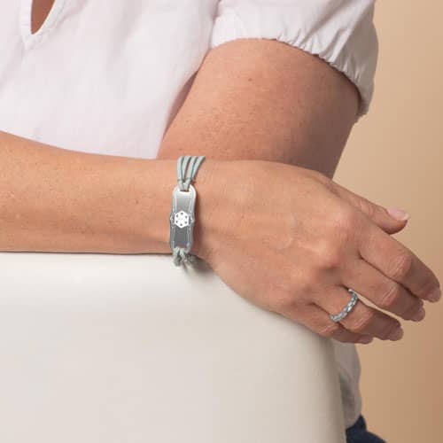 Woman displaying the engraved back of a light blue wrap-style medical ID bracelet, showing personalized medical information for emergency responders.
