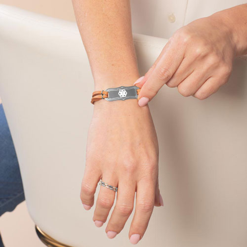 Woman wearing Avery SmartSize Medical ID Bracelet with suede copper tone leather band and adjustable chain, with a silver La Petite tag with a white Cadeusus