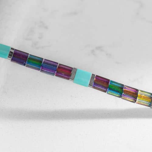 Close-up of Twilight bracelet beads showcasing shimmering iridescent tiles, aqua accents, and polished metal spacers.