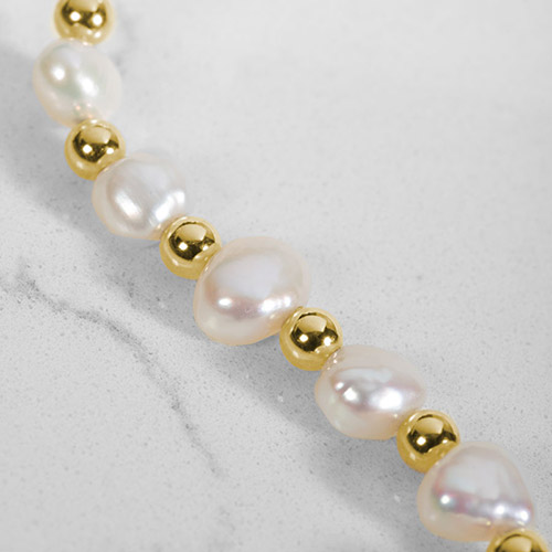 Close-up of freshwater pearl and gold bead medical ID bracelet strand with luminous natural pearl detail.