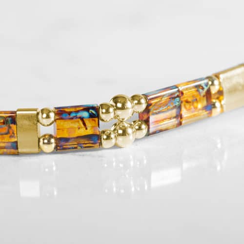 Close-up of amber-toned rectangular bracelet accents with gold-tone spacers and decorative round bead details on a white background.