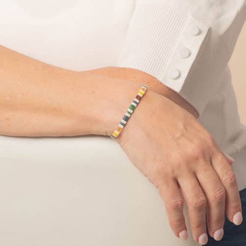 Colorful tiled medical ID bracelet with white, slate blue, green, yellow, and amber accents worn on the wrist.