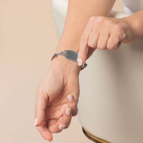 Person displaying the engraved back of a silver-tone medical ID bracelet on the wrist.