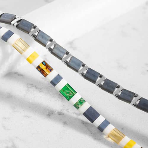 Close-up of colorful tiled medical ID bracelet links in white, slate blue, green, yellow, and amber tones.