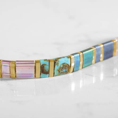 Close-up of rectangular bracelet beads in pink, aqua, blue, and iridescent tones separated by gold-tone accents.