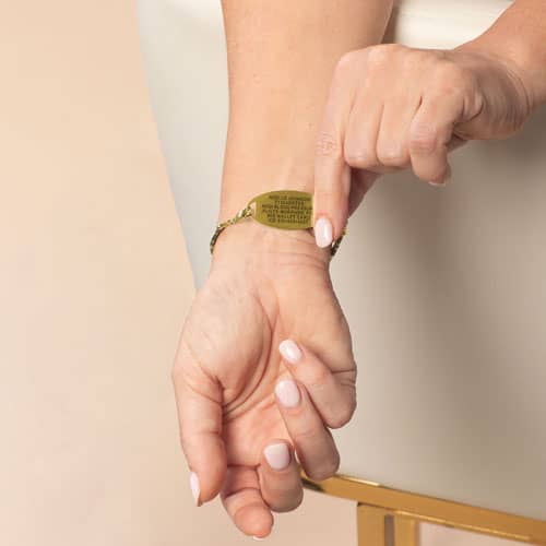 Model is wearing a gold-tone medical ID bracelet while displaying the engraved medical information on the back of the tag.