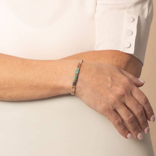Model is wearing a slim gold-tone bracelet with colorful rectangular beads in aqua, blue, pink, and clear tones.