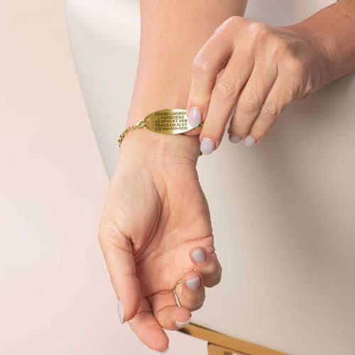 Model is wearing a gold-tone medical ID bracelet while displaying the engraved medical information on the back of the tag.