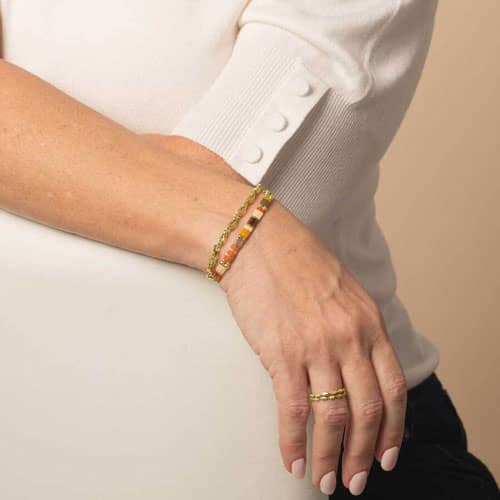 Model is wearing a three-strand gold-tone bracelet featuring colorful rectangular beads in orange, cream, brown, green, and red.