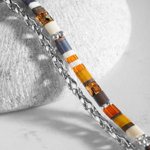 Close-up of colorful rectangular beads in orange, yellow, cream, brown, and blue alongside a silver-tone chain.