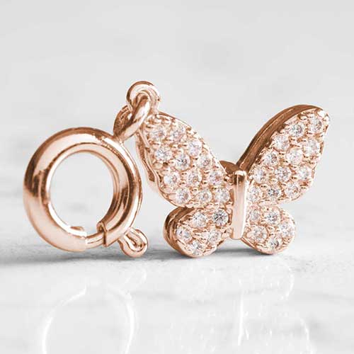 Crystal in lays sparkle on a rose gold, butterfly shaped charm, sitting atop white marble.