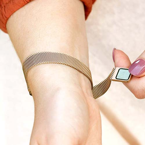 Woman opening mesh chain band with magnetic closure on brushed sandstone plated stainless Urban Medical Alert bracelet.