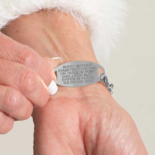 Woman in white sweater wearing silver tone bar link chain bracelet with blush mother of pearl inlay showing premium laser engraving.