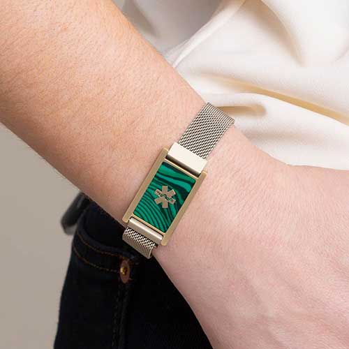 Woman wearing brushed sandstone, stainless steel mesh band with imitation malachite and gold tone medical symbol.