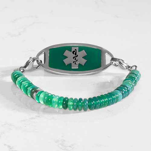 Jade Heishi beaded Bracelet with silver lobster clasps, attached to a silver and emerald decorative medical ID tag with silver caduceus, on white marble.