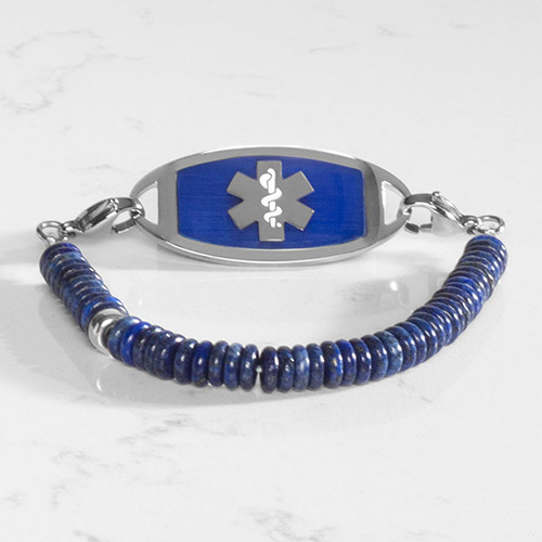 Blue Lapis heshi beaded medical ID bracelet on jewelry elasticwith silver tone lobster clasps and lapis inlaid silver tone med ID tag, on white marble.