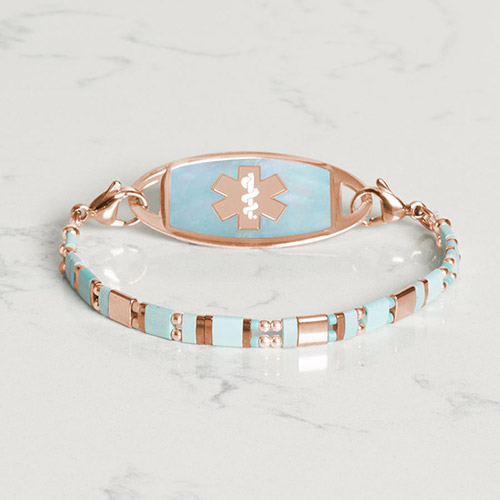 Flat lay of a rose mother-of-pearl medical ID bracelet with an adjustable metal chain, combining elegance with essential medical safety.