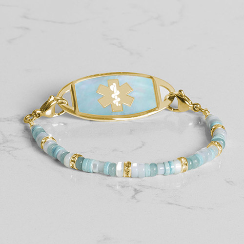 Flat lay of a gold medical ID bracelet with a blue mother-of-pearl inlay, showcasing its elegant design and safety features.
