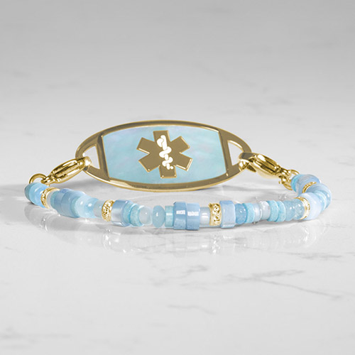 Flat lay of a gold medical ID bracelet with a blue mother-of-pearl inlay, showcasing its elegant design and safety features.