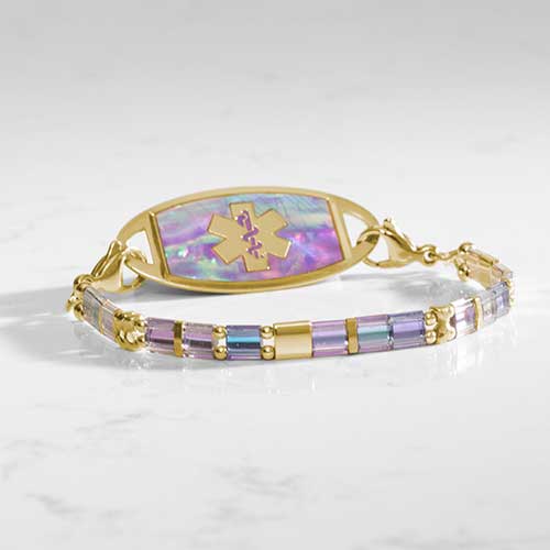 Gold medical ID bracelet with pastel iridescent beads and engraved medical alert tag, inlaid with lilac abalone, on white marble.