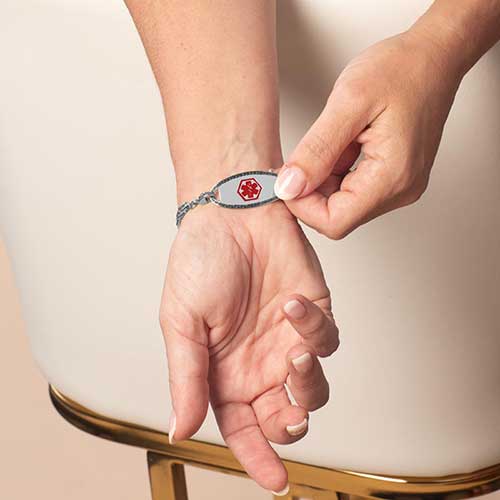 Woman displaying stainless steel medical ID tag with red medical alert symbol.