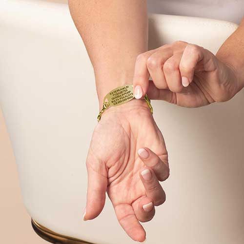Woman displaying custom laser engraving on her gold ton stainless steel medical alert ID tag.