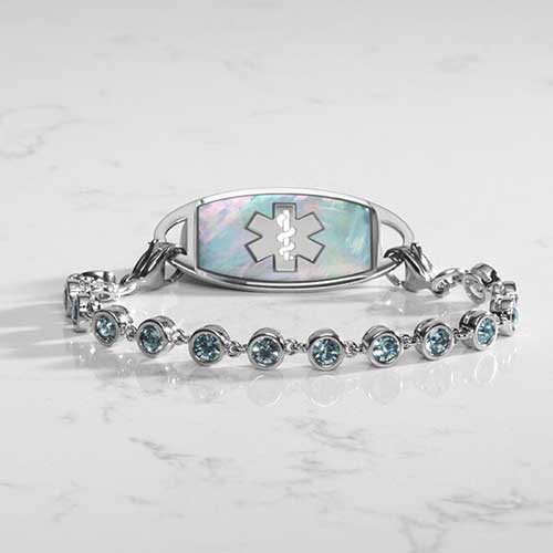 Rhodium and palladium plated women's medical alert bracelet with aquamarine tone, round, bezel set cubic zirconia crystals paired with stainless steel and mother of pearl medical ID tag.