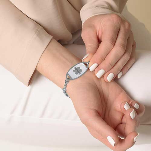 Woman displaying stainless steel medical ID tag with Mother of Pearl inlay and silver medical alert symbol.