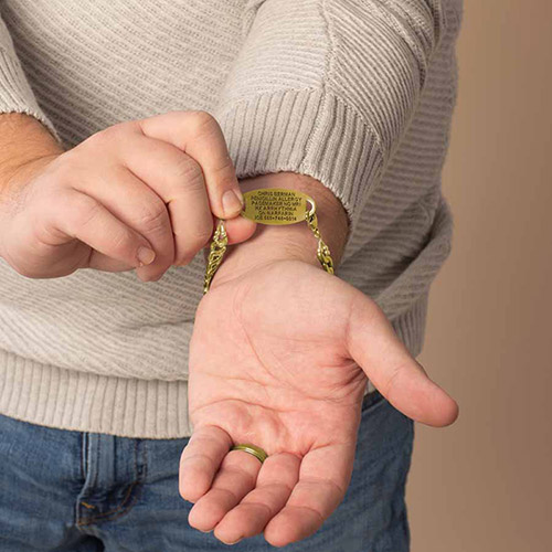Man wearing a gold medical ID bracelet with visible engraving showing emergency information, demonstrating how the bracelet fits on the wrist.
