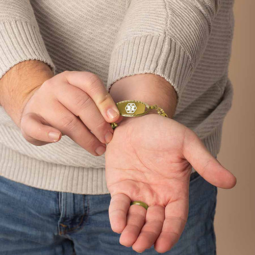 Man holding up the front of his gold medical ID bracelet featuring a white medical symbol on a gold face, highlighting emergency alert visibility.