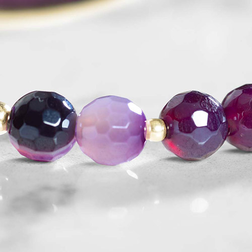 The same purple ombré faceted bracelet strand styled with silver lobster clasps, displayed on a reflective white surface.