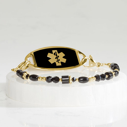 Livi in Black Gold interchangeable medical ID bracelet shown with a glossy black ID tag and gold caduceus, displayed on a white pedestal.