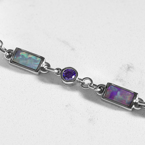 Detailed view of rectangular lilac abalone inlays and round violet CZ stones in a silver bracelet link setting.