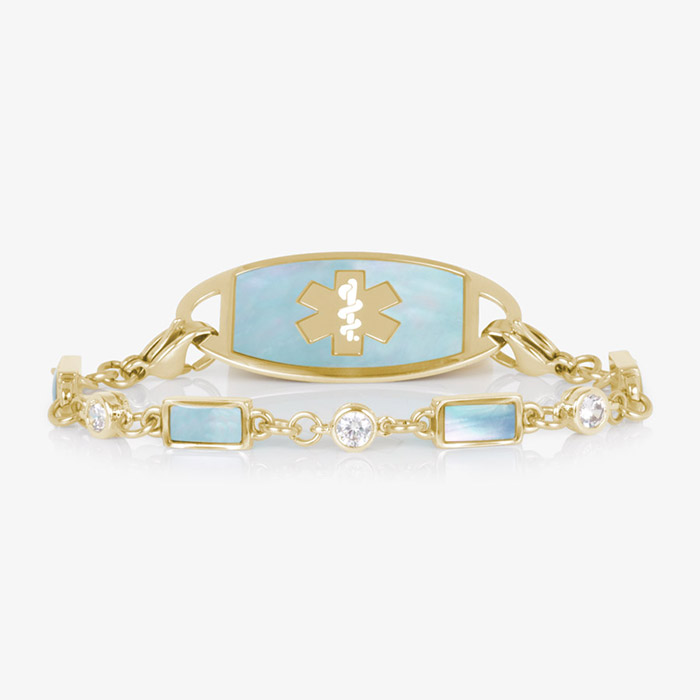 Gold medical ID bracelet with light blue mother-of-pearl inlay and crystal accents, featuring an engraved medical caduceus symbol on the ID tag.