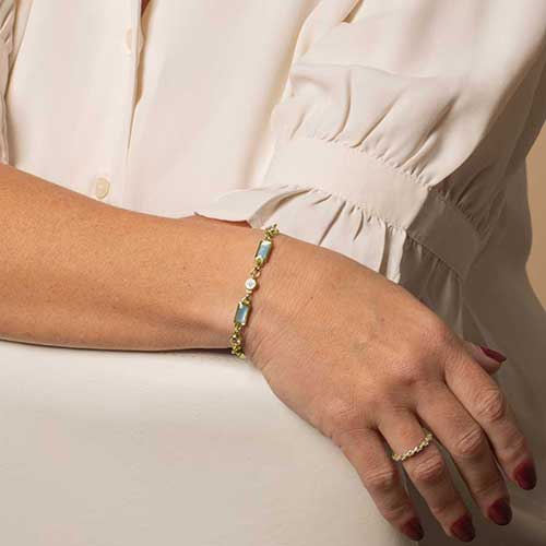 Woman wearing a gold tone bracelet featuring alternating crystal and blue mother of pearl links