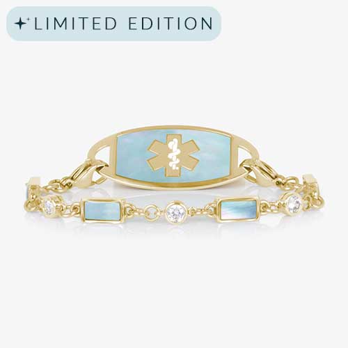 Gold medical ID bracelet with light blue mother-of-pearl inlay and crystal accents, featuring an engraved medical caduceus symbol on the ID tag.