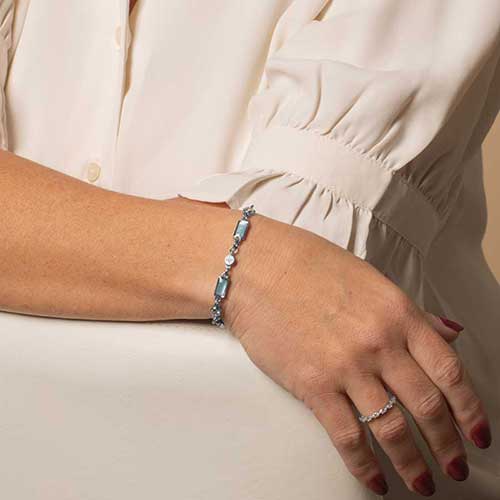 Woman wearing a silver tone bracelet featuring alternating crystal and blue mother of pearl links.