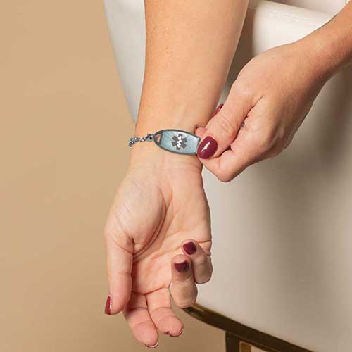 Woman displayingher silver medical ID tag, featuring blue mother of pearl inlay and a silver medical ID symbol.