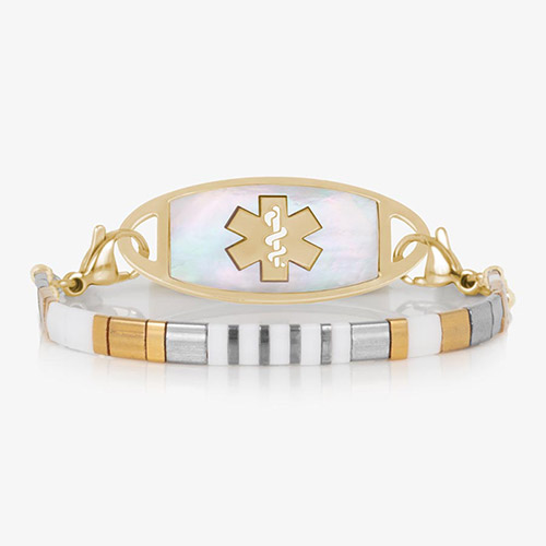 Front view of a gold medical ID bracelet featuring a mother-of-pearl tag and a slim, striped tile band with alternating white, silver, and gold tones.