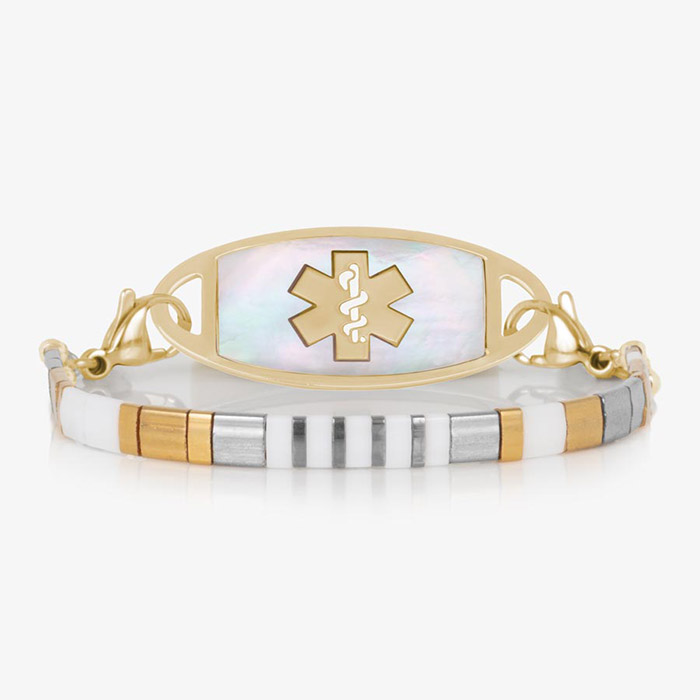 Front view of a gold medical ID bracelet featuring a mother-of-pearl tag and a slim, striped tile band with alternating white, silver, and gold tones.