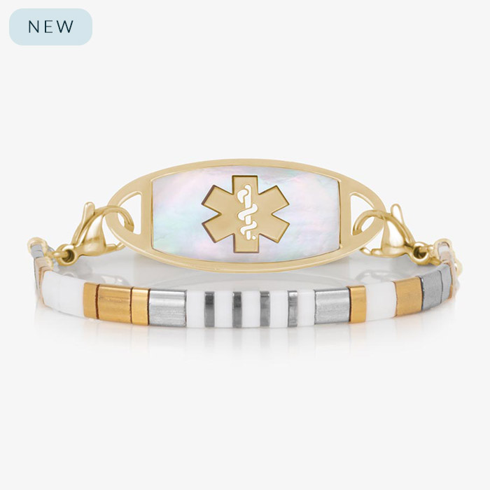 Front view of a gold medical ID bracelet featuring a mother-of-pearl tag and a slim, striped tile band with alternating white, silver, and gold tones.