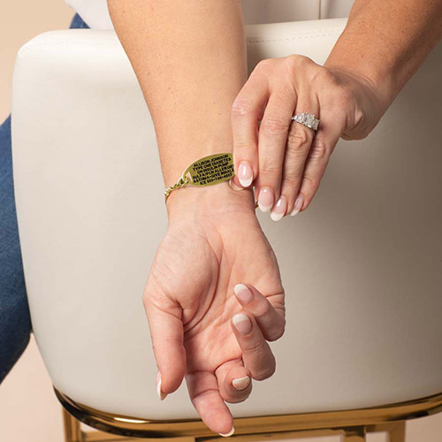 Woman showing the underside of the Nova Gold medical ID bracelet, displaying the custom engraved medical information on a gold tag.