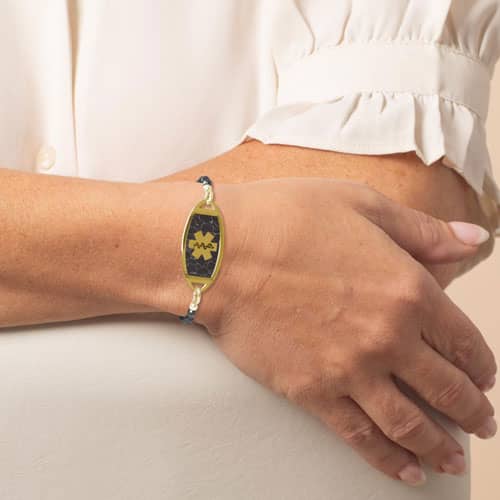 Woman wearing a gold medical ID bracelet with black beaded chain and marble inlay, combining elegant style with safety.