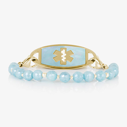 Gold medical ID bracelet with pale blue faceted gemstone beads and gold accent spacers, shown with a matching gold ID tag featuring a cloud blue inlay and cutout medical symbol.