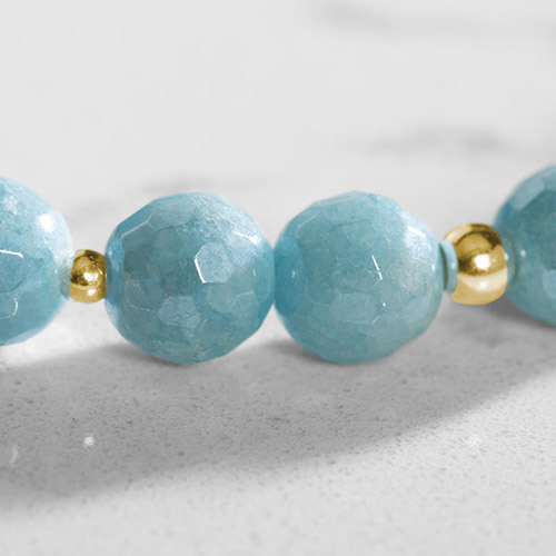 Macro detail of pale blue faceted gemstone beads and gold spacers, highlighting texture and color variation in the bracelet strand.