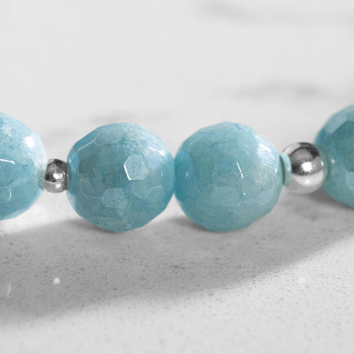 Macro image of aquamarine beads with silver spacer beads, highlighting their faceted texture and subtle color shifts.