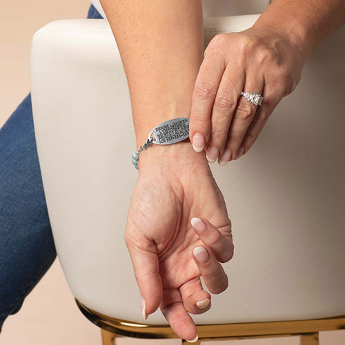 Model wearing a Lauren’s Hope medical ID bracelet with a silver tag engraved with emergency details and a light blue beaded stretch strand.