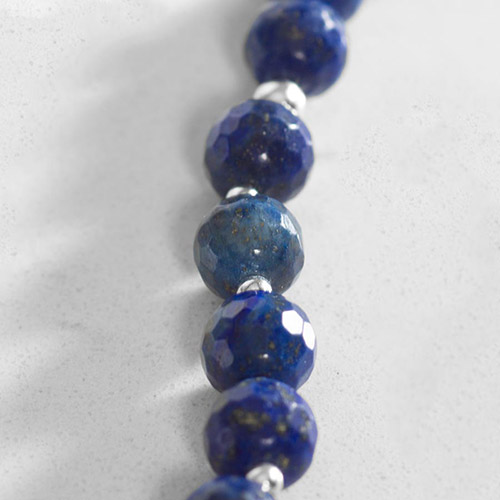 Close-up of faceted denim lapis beads with natural gold flecks and striations, separated by small silver spacer beads.