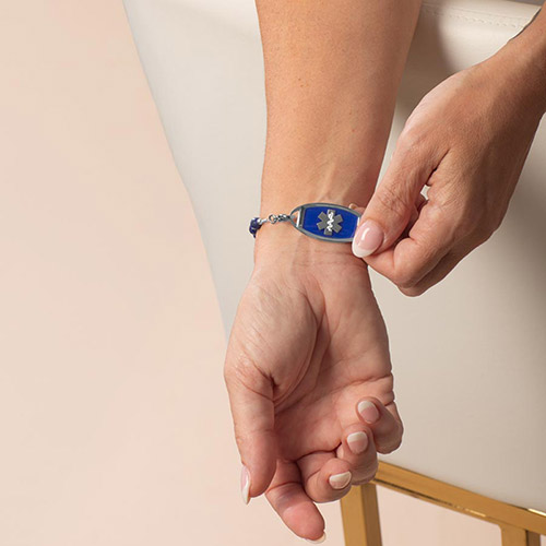 Model holding wrist out to display the silver-tone medical ID tag with a cobalt blue face and silver medical symbol.